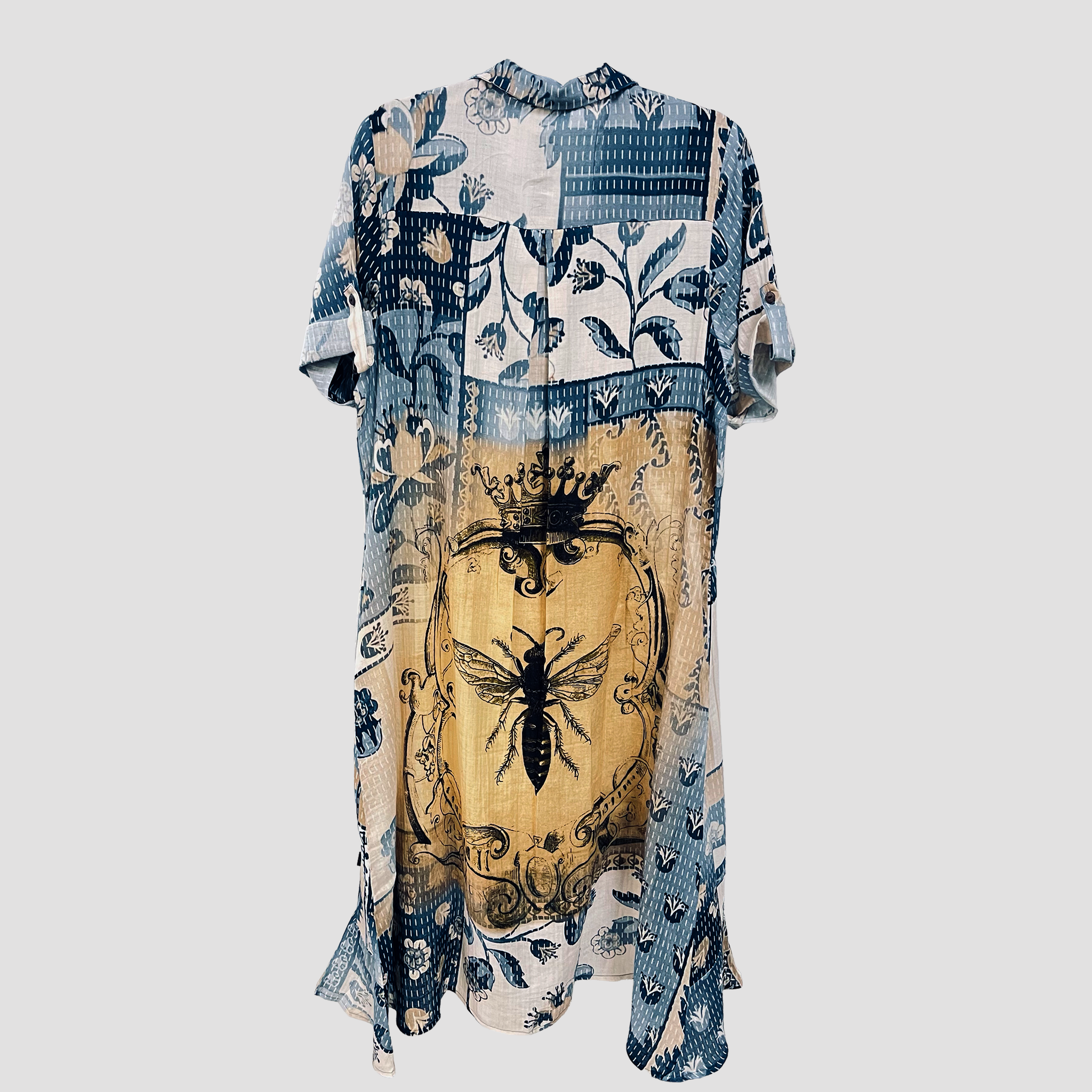 A short-sleeve, high-low hem dress featuring a patchwork print of blue floral motifs, a central gold shield with a black bee, and a crown, shown against a light gray background.